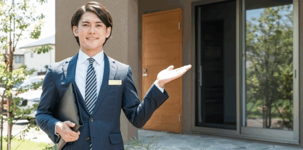 スーツ姿の男性営業スタッフが住宅前で案内している様子。