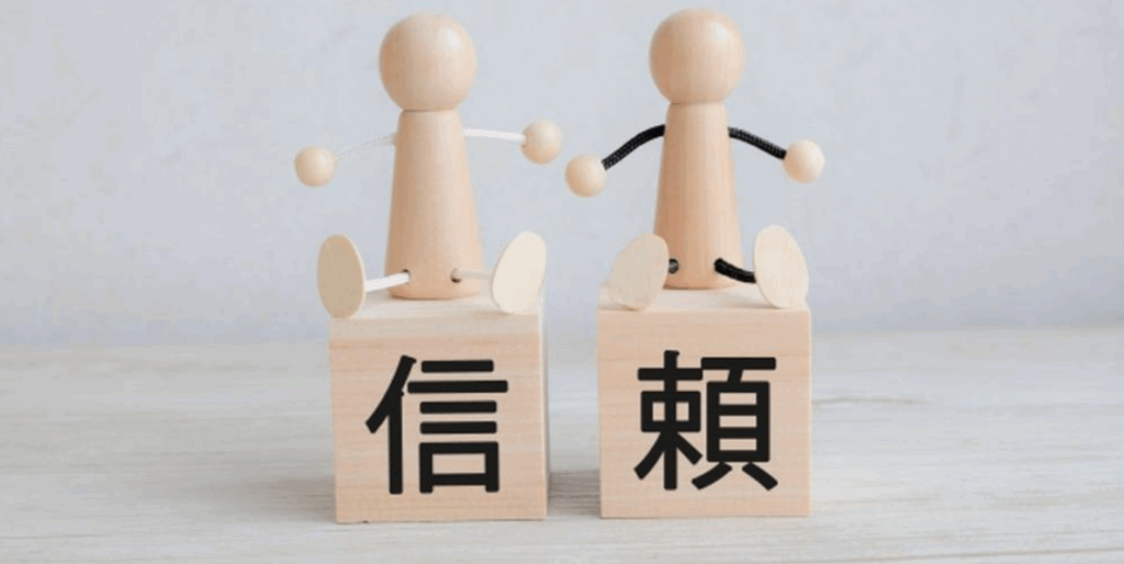 『信頼』と書かれた木のブロックの上に座る木製の人形2体、信頼関係のイメージ